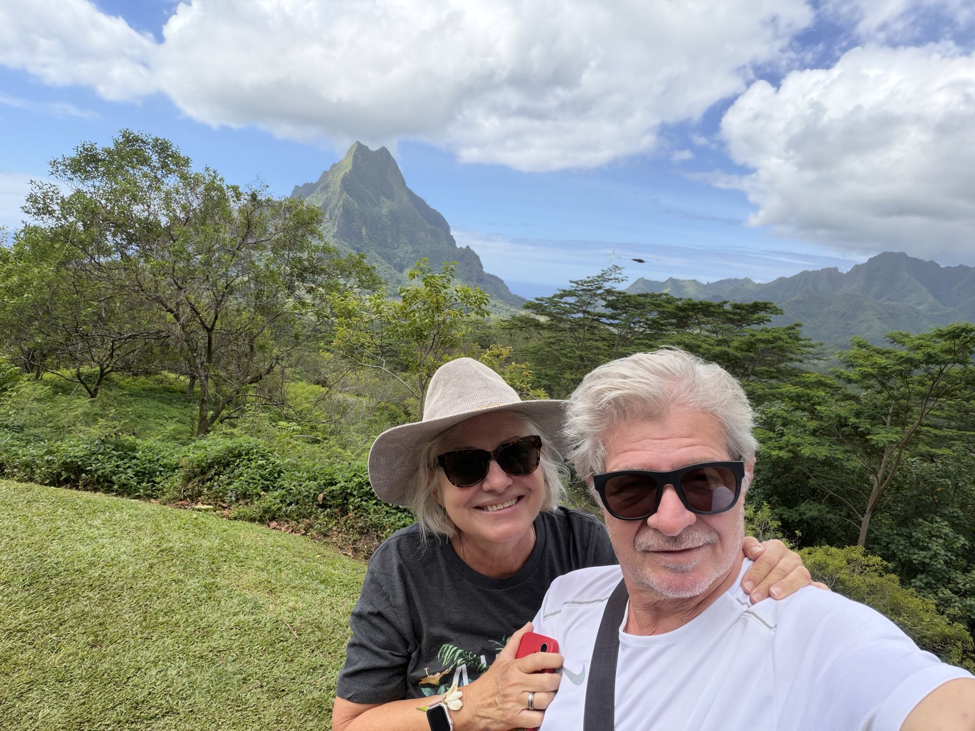 Alex and Leigh-Ann smiling at a lookout, with a green mountain peak and blue sky behind them