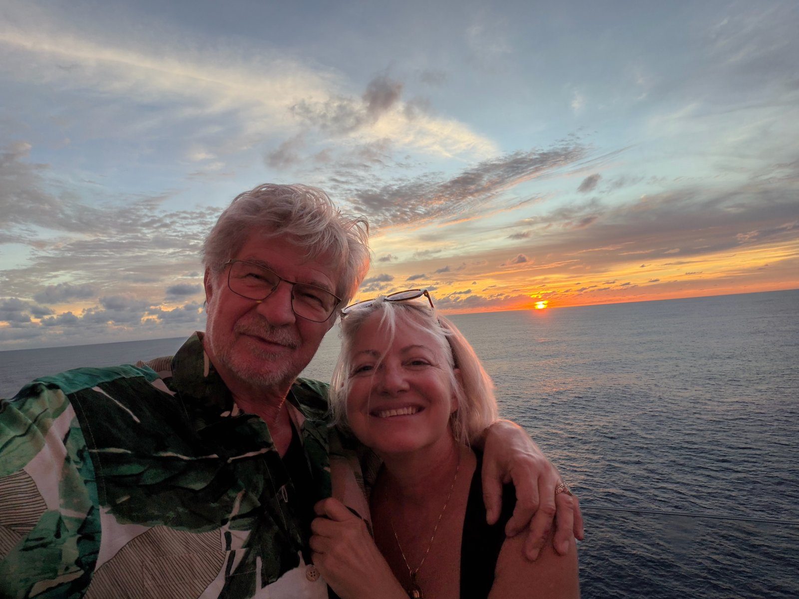 Alex and Leigh-Ann smiling together at sea as the sun sets over the ocean